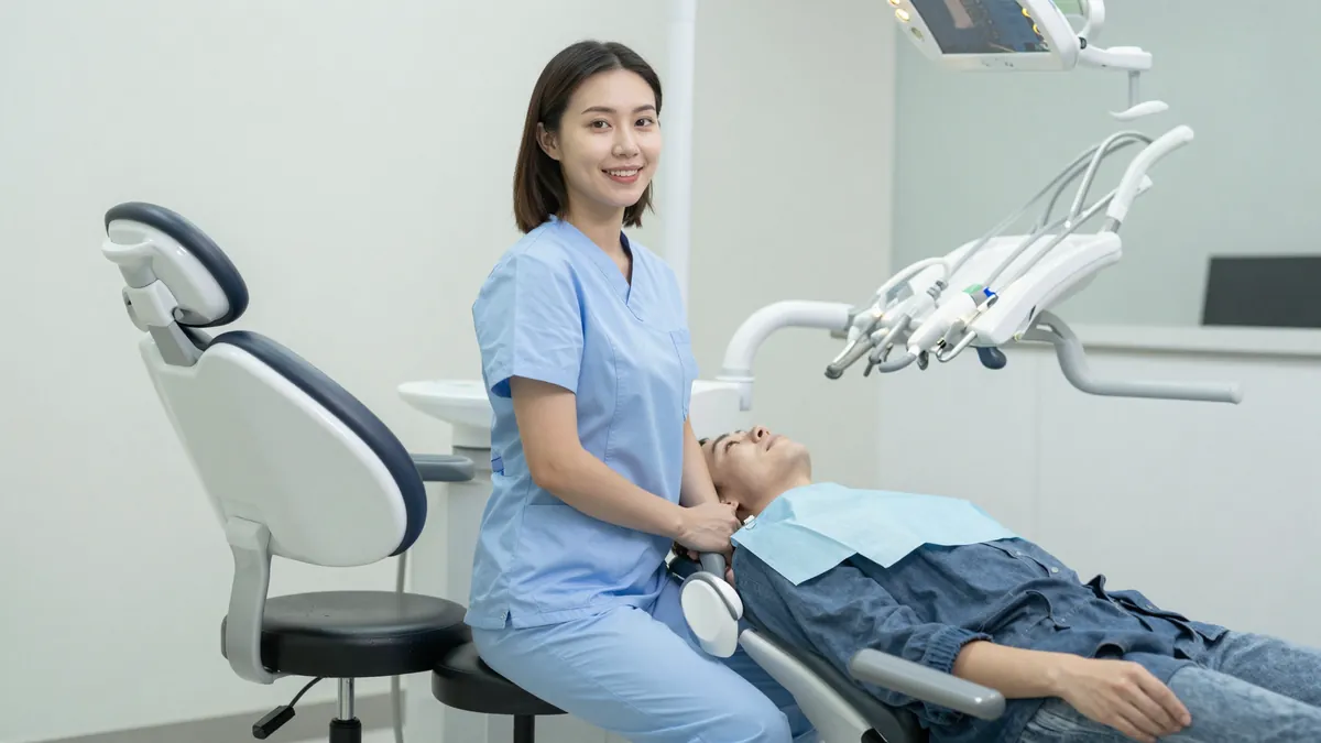 Dental hygienist seated on a saddle stool at correct working height beside a patient